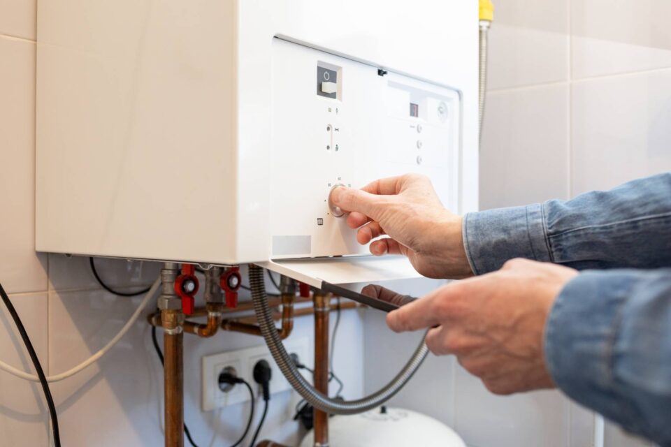 Technician adjusting a boiler temperature dial with visible plumbing in San Joaquin County