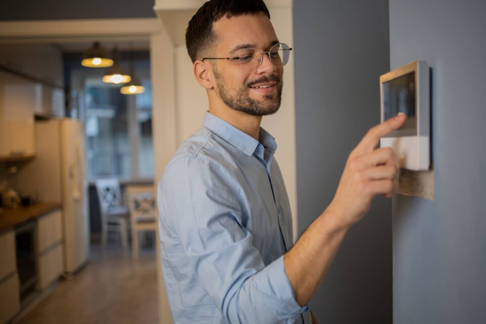Man adjusting a smart thermostat on a grey wall in a modern home in San Joaquin County