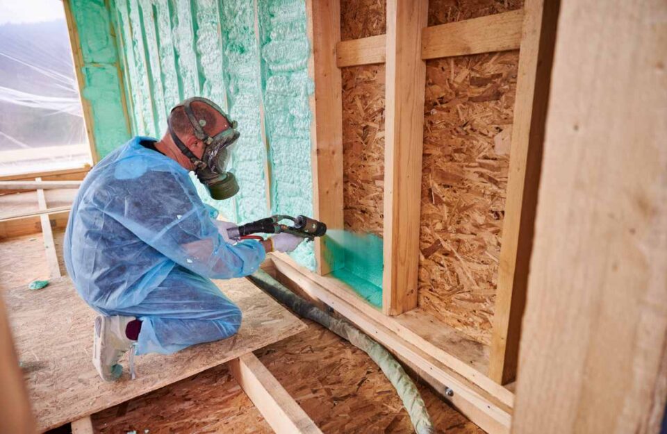 Worker applying green spray foam insulation to a wall cavity in San Joaquin County