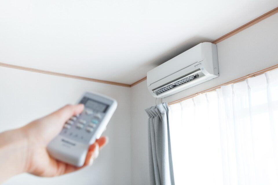 Hand holding a remote control aimed at a wall-mounted air conditioner in San Joaquin County