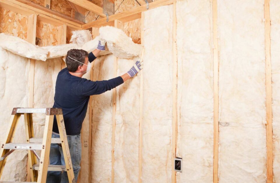 Construction worker installing batt insulation into a wooden wall frame in San Joaquin County